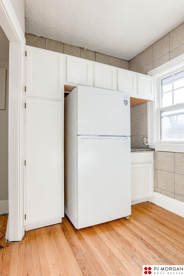 kitchen featuring white fridge, white cabinets, light wood-type flooring, and a textured ceiling