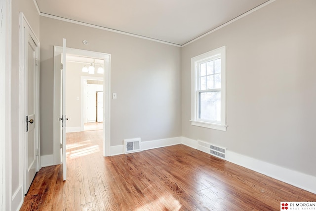 empty room with an inviting chandelier, ornamental molding, and hardwood / wood-style floors