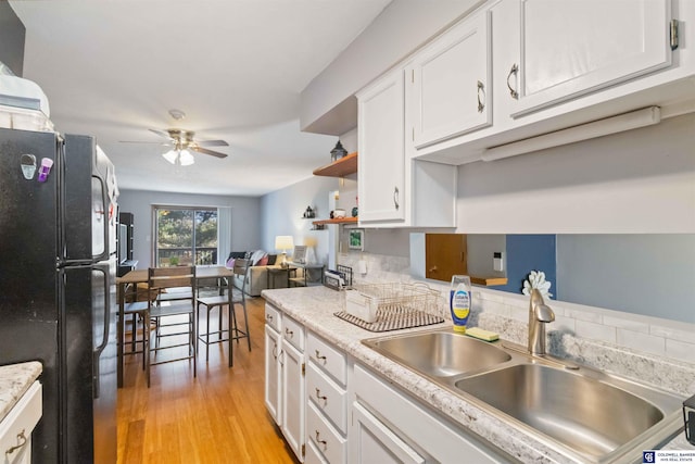 kitchen with black fridge, white cabinets, sink, and light hardwood / wood-style flooring