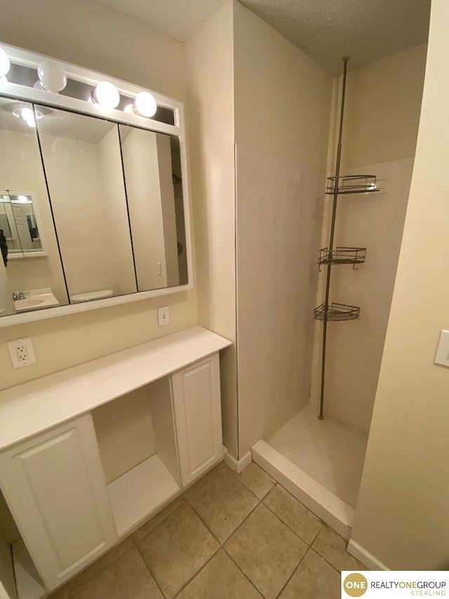 bathroom featuring tile patterned flooring, vanity, a textured ceiling, and walk in shower