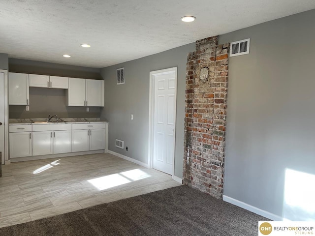 kitchen featuring light carpet, a textured ceiling, white cabinets, and sink