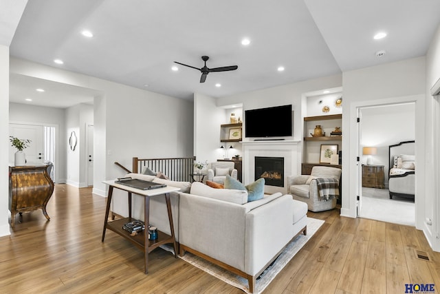 living room with light hardwood / wood-style floors, ceiling fan, and built in shelves