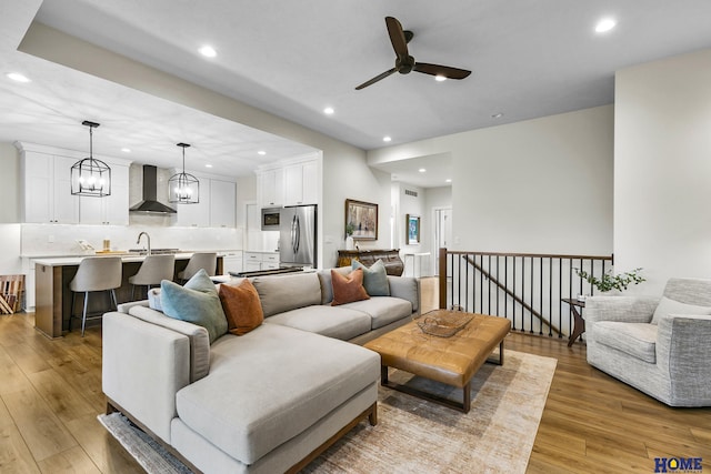 living room featuring ceiling fan with notable chandelier, sink, and light wood-type flooring