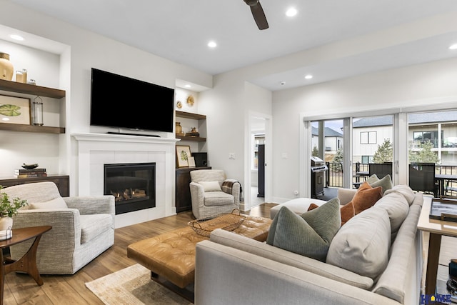 living room featuring a tile fireplace, light wood-type flooring, ceiling fan, and built in features