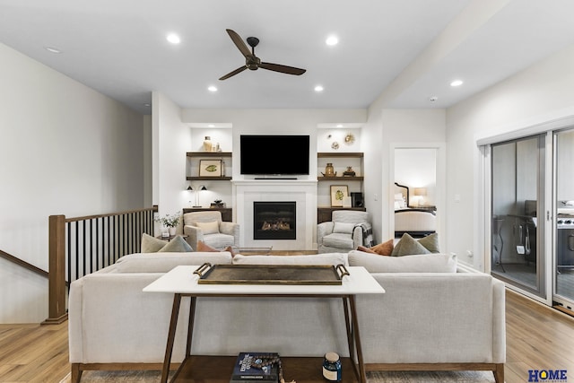 living room with light wood-type flooring, ceiling fan, and built in features