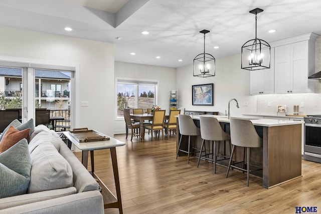 kitchen with white cabinetry, light hardwood / wood-style floors, an island with sink, hanging light fixtures, and stainless steel range