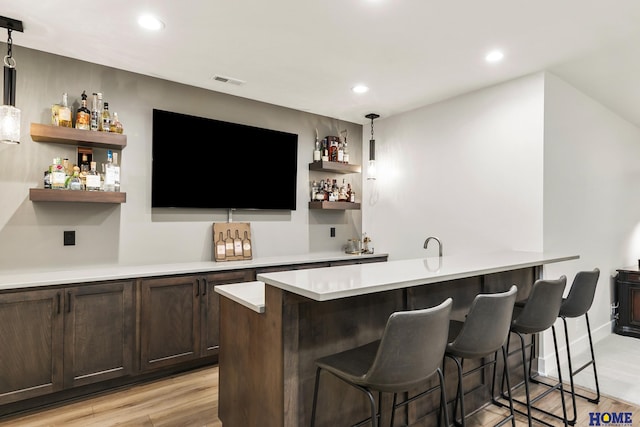 bar featuring decorative light fixtures, light hardwood / wood-style floors, and dark brown cabinetry