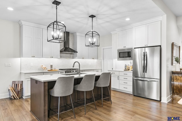 kitchen featuring appliances with stainless steel finishes, white cabinets, wall chimney range hood, and sink