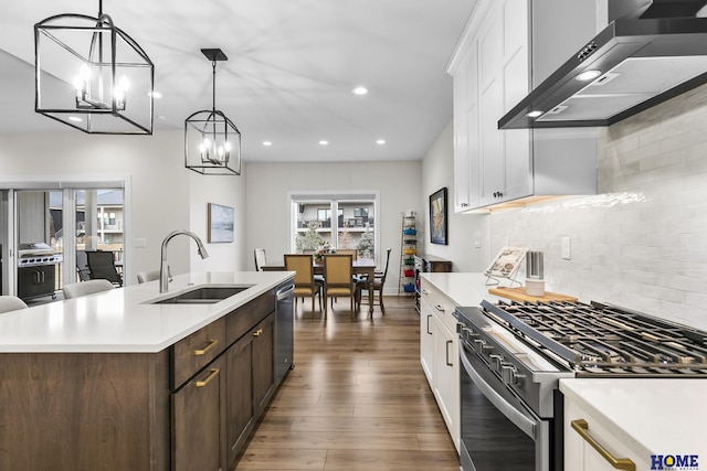 kitchen featuring wall chimney exhaust hood, a kitchen island with sink, white cabinets, appliances with stainless steel finishes, and sink