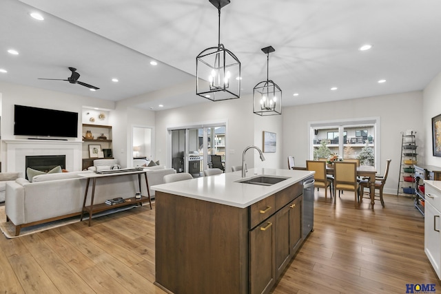 kitchen featuring sink, stainless steel dishwasher, ceiling fan with notable chandelier, a center island with sink, and pendant lighting