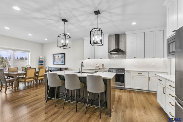 kitchen with white cabinets, stainless steel gas range, wall chimney exhaust hood, sink, and decorative light fixtures