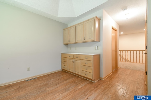 kitchen featuring a textured ceiling, light wood-type flooring, and light brown cabinetry