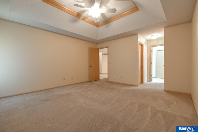 carpeted spare room with ornamental molding, ceiling fan, a textured ceiling, and a tray ceiling