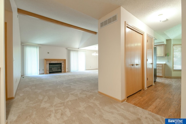 unfurnished living room featuring light carpet, lofted ceiling with beams, a textured ceiling, and a notable chandelier