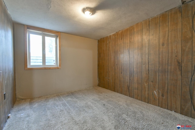 unfurnished room featuring a textured ceiling, wooden walls, and carpet flooring