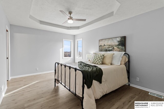 bedroom with a raised ceiling, wood-type flooring, a textured ceiling, and ceiling fan