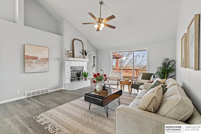 living room with a tiled fireplace, hardwood / wood-style floors, high vaulted ceiling, and ceiling fan