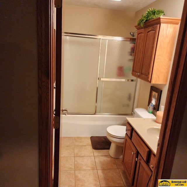 full bathroom with a textured ceiling, tile patterned flooring, vanity, bath / shower combo with glass door, and toilet