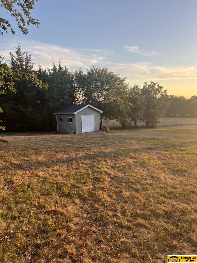 yard at dusk with a garage, a rural view, and an outdoor structure