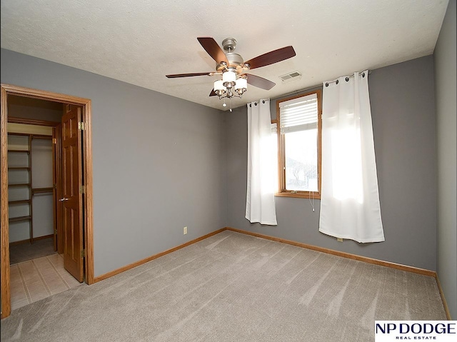 empty room with a textured ceiling, ceiling fan, and light colored carpet