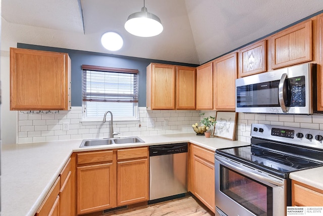 kitchen with vaulted ceiling, stainless steel appliances, light wood-type flooring, sink, and tasteful backsplash