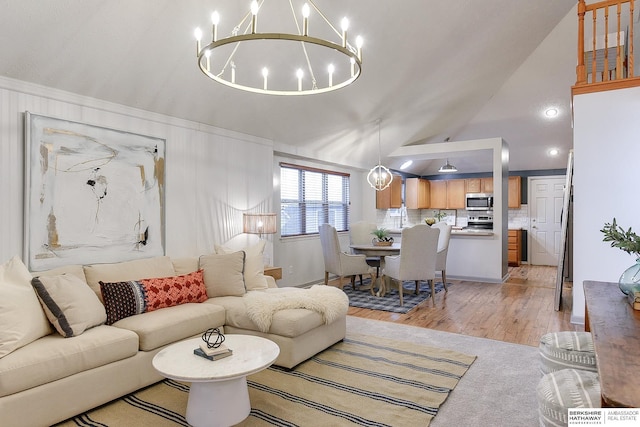 living room with lofted ceiling, an inviting chandelier, and light wood-type flooring