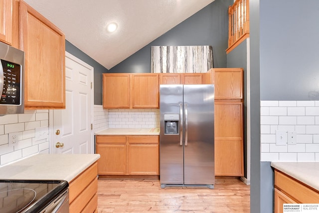 kitchen featuring stainless steel appliances, vaulted ceiling, light wood-type flooring, and tasteful backsplash