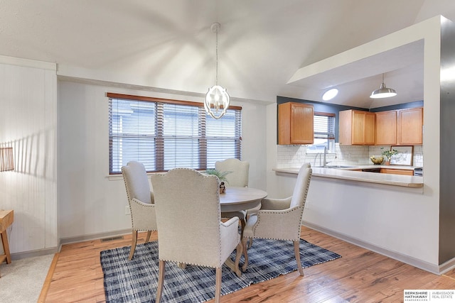 dining area with lofted ceiling, sink, an inviting chandelier, and light wood-type flooring