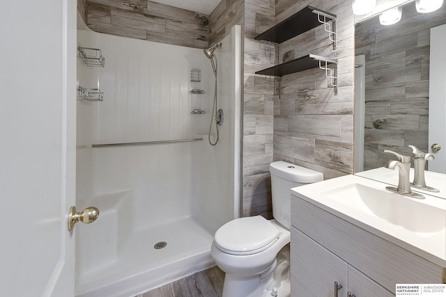 bathroom with toilet, hardwood / wood-style flooring, walk in shower, tile walls, and vanity