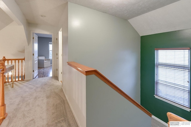 hallway featuring a textured ceiling, vaulted ceiling, and light colored carpet