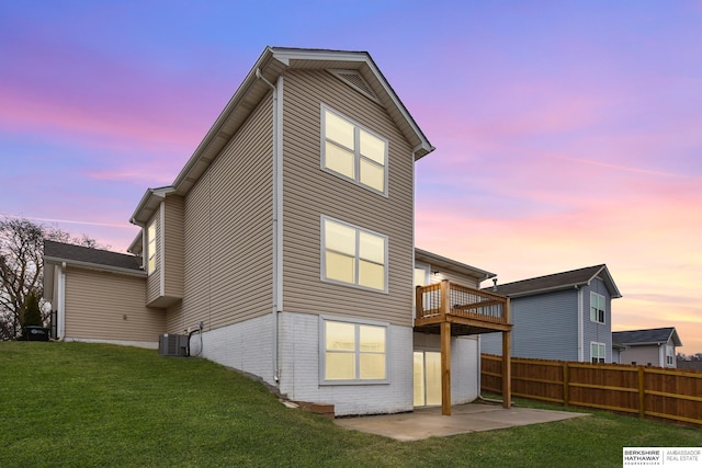 back house at dusk featuring a lawn, central air condition unit, a balcony, and a patio