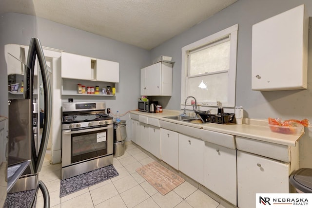 kitchen with black refrigerator, a textured ceiling, stainless steel range with gas cooktop, white cabinets, and light tile patterned flooring