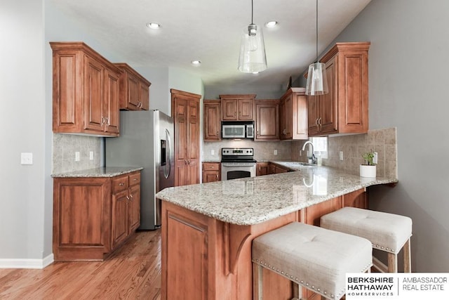 kitchen with a breakfast bar area, appliances with stainless steel finishes, sink, decorative light fixtures, and tasteful backsplash