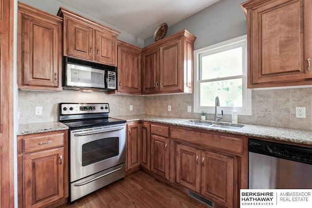 kitchen featuring light stone counters, dark wood-type flooring, stainless steel appliances, backsplash, and sink