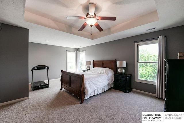 carpeted bedroom featuring ceiling fan and a raised ceiling