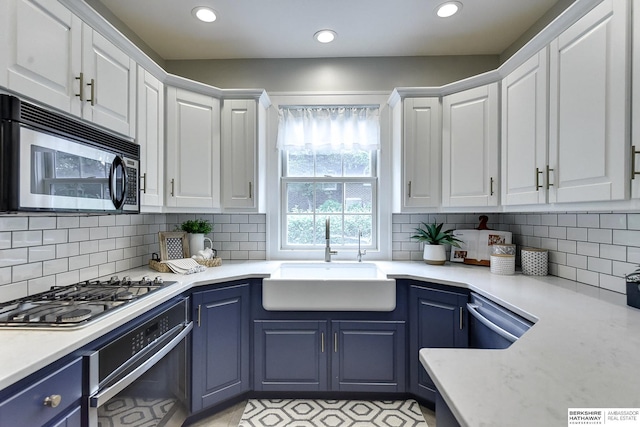 kitchen with stainless steel appliances, blue cabinetry, sink, white cabinetry, and tasteful backsplash