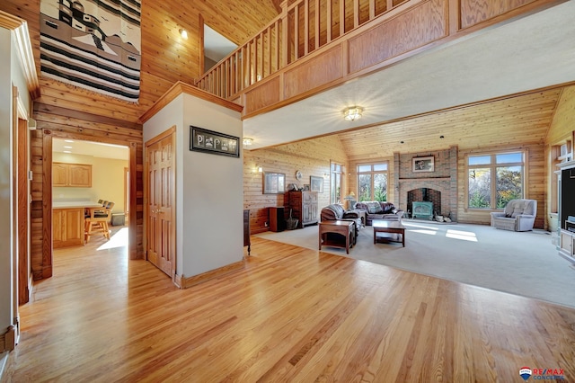 living room with light wood-type flooring, wooden walls, high vaulted ceiling, and a fireplace