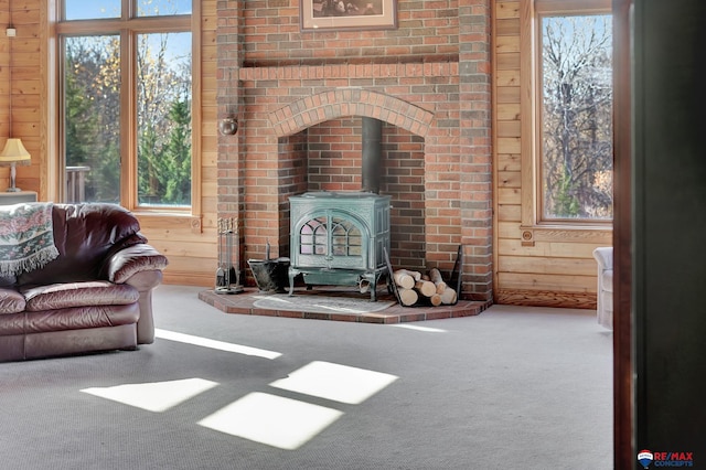 living room with carpet flooring, a healthy amount of sunlight, wooden walls, and a wood stove