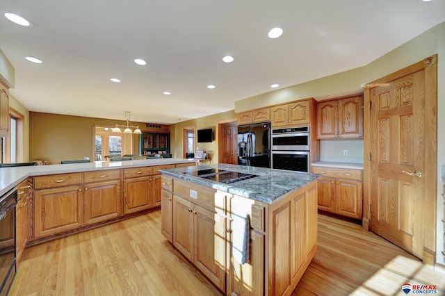 kitchen with decorative light fixtures, light hardwood / wood-style floors, black appliances, a kitchen island, and dark stone countertops