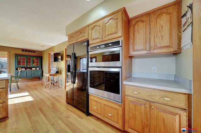 kitchen featuring black fridge, double oven, and light wood-type flooring