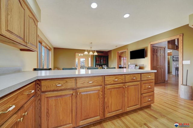 kitchen with decorative light fixtures, light hardwood / wood-style floors, and kitchen peninsula