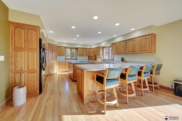 kitchen featuring a kitchen breakfast bar, kitchen peninsula, black fridge, sink, and light hardwood / wood-style flooring