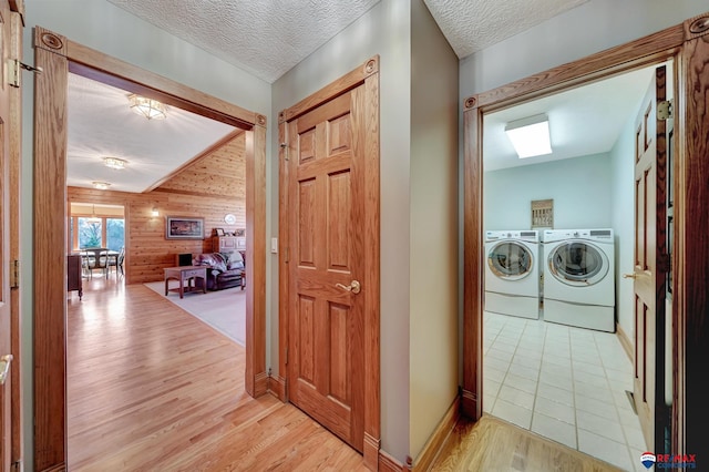 washroom with a textured ceiling, wood walls, washing machine and clothes dryer, and light hardwood / wood-style floors