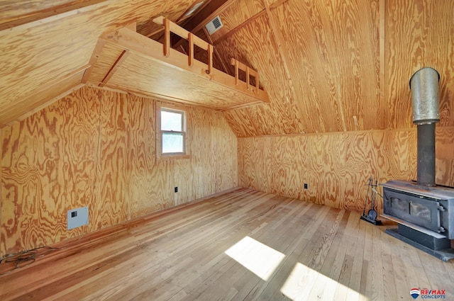 additional living space with hardwood / wood-style floors, wooden walls, vaulted ceiling, and a wood stove