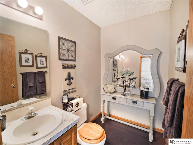 bathroom with a textured ceiling, vanity, and toilet