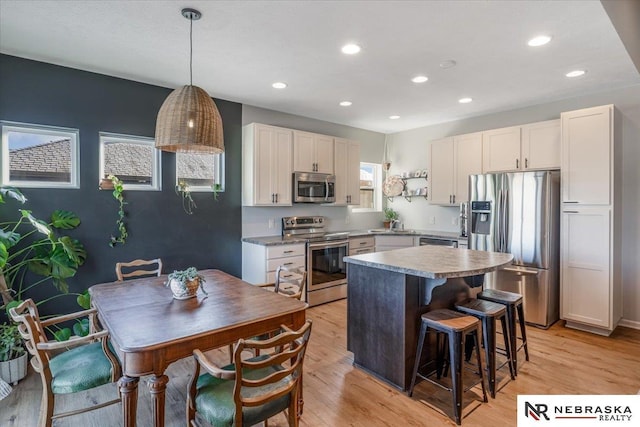 kitchen with stainless steel appliances, white cabinetry, a center island, and light hardwood / wood-style flooring