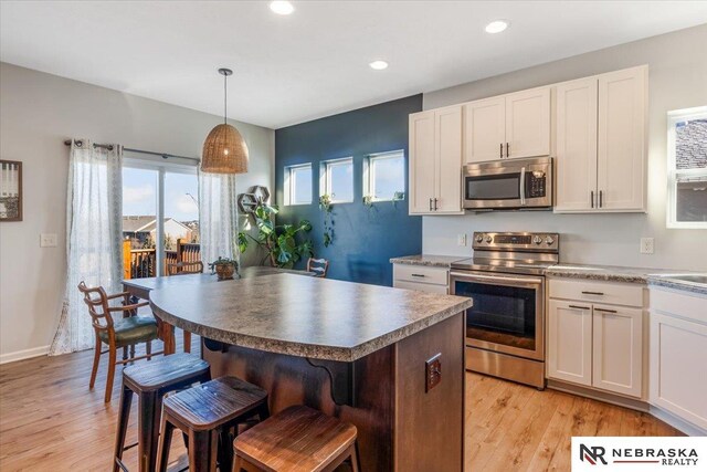 kitchen featuring stainless steel appliances, white cabinetry, decorative light fixtures, and light wood-type flooring