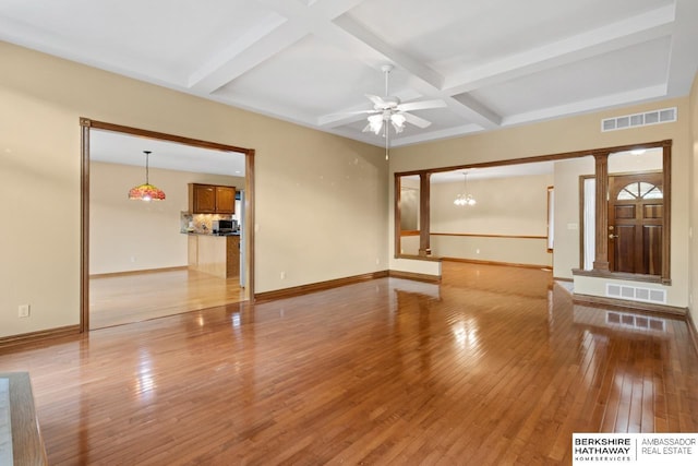 unfurnished living room featuring ceiling fan with notable chandelier, light wood-type flooring, beam ceiling, and coffered ceiling