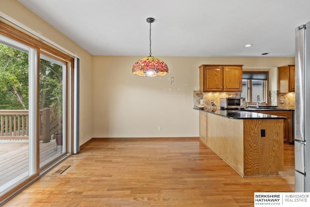 kitchen featuring dark stone countertops, tasteful backsplash, light hardwood / wood-style flooring, kitchen peninsula, and hanging light fixtures