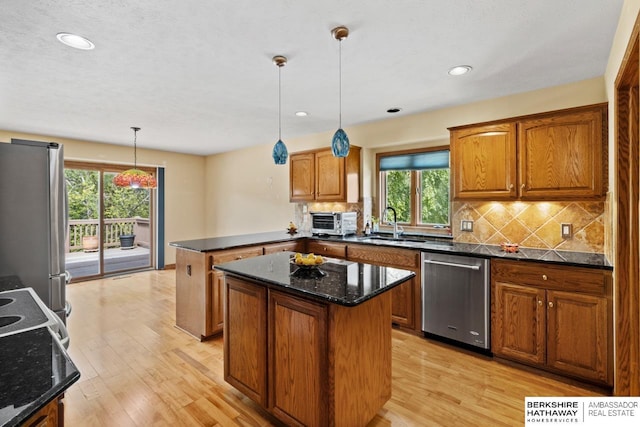 kitchen with appliances with stainless steel finishes, hanging light fixtures, backsplash, and a kitchen island